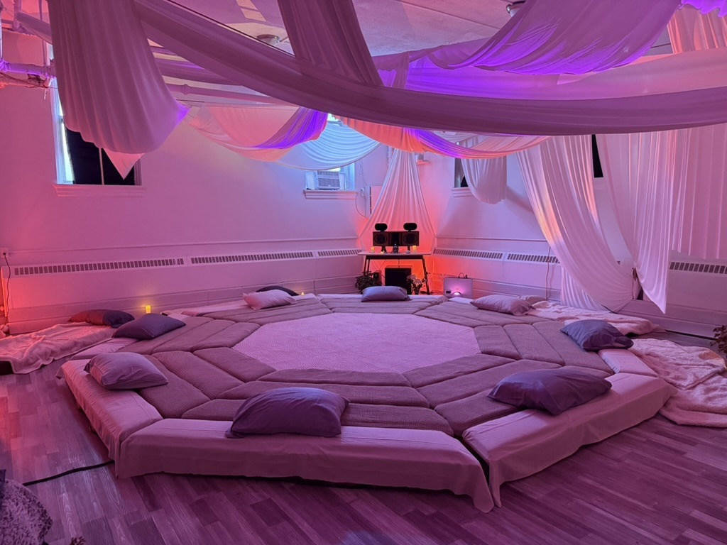 The Greenpoint room lit in pink and violet: the octagon platform ringed with cushions under draped ceiling fabric, nobody on it.