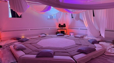 The Greenpoint room lit in pink and violet: the octagon platform ringed with cushions under draped ceiling fabric, no one on it.