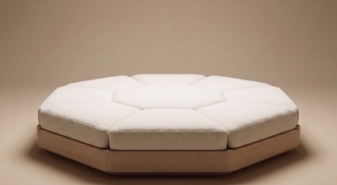 AVA, the audio visual artifact: the octagon haptic platform in bone upholstery on an oak base, photographed alone on a plain warm ground.