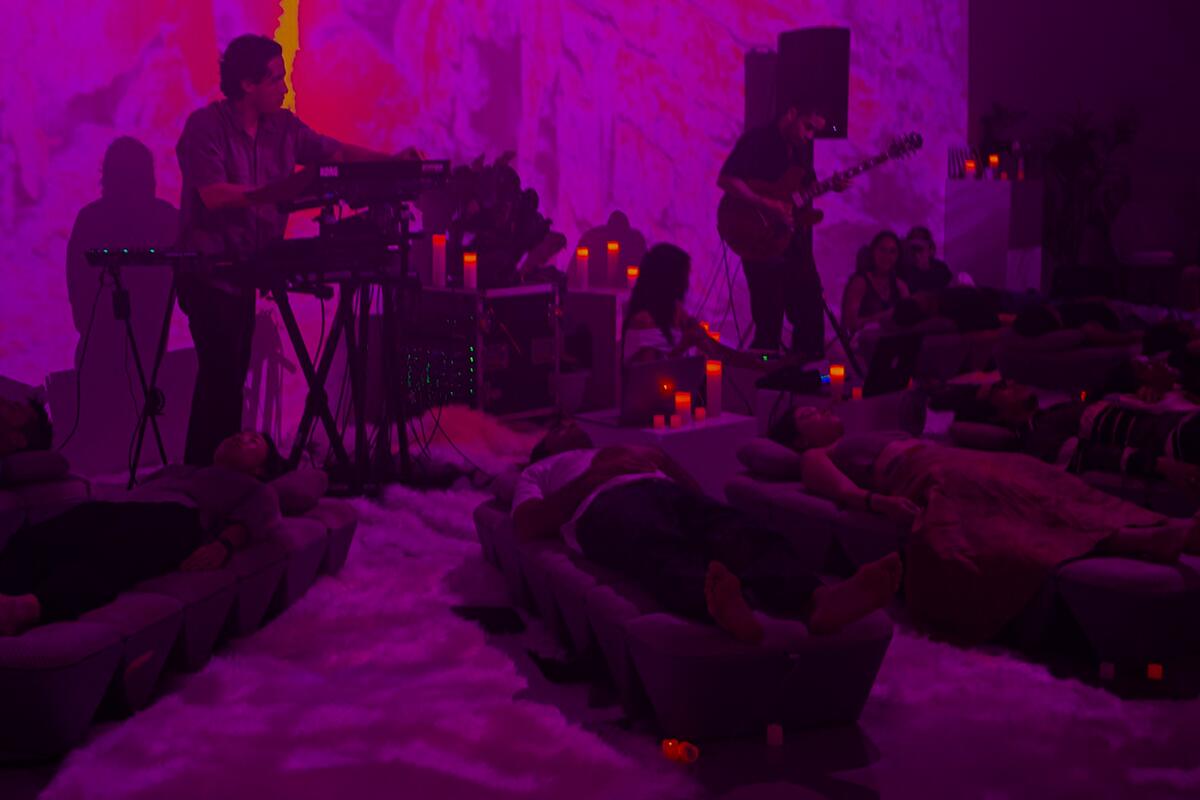 A live set in the SoundTemple room under magenta light, players at the far wall, guests reclined around AVA.