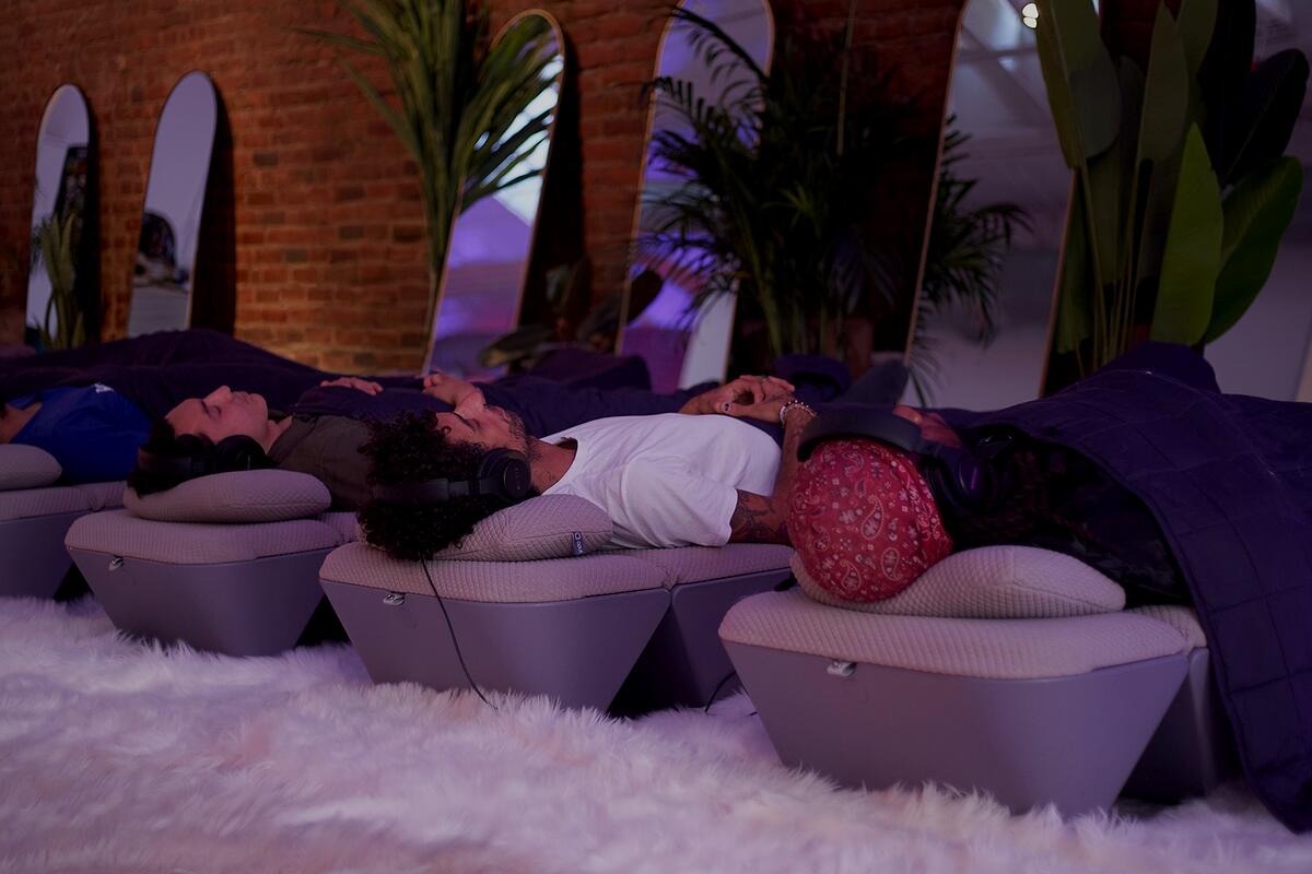 Daylight in the SoundTemple room: guests resting on the loungers against the brick wall, plants and mirrors behind them.