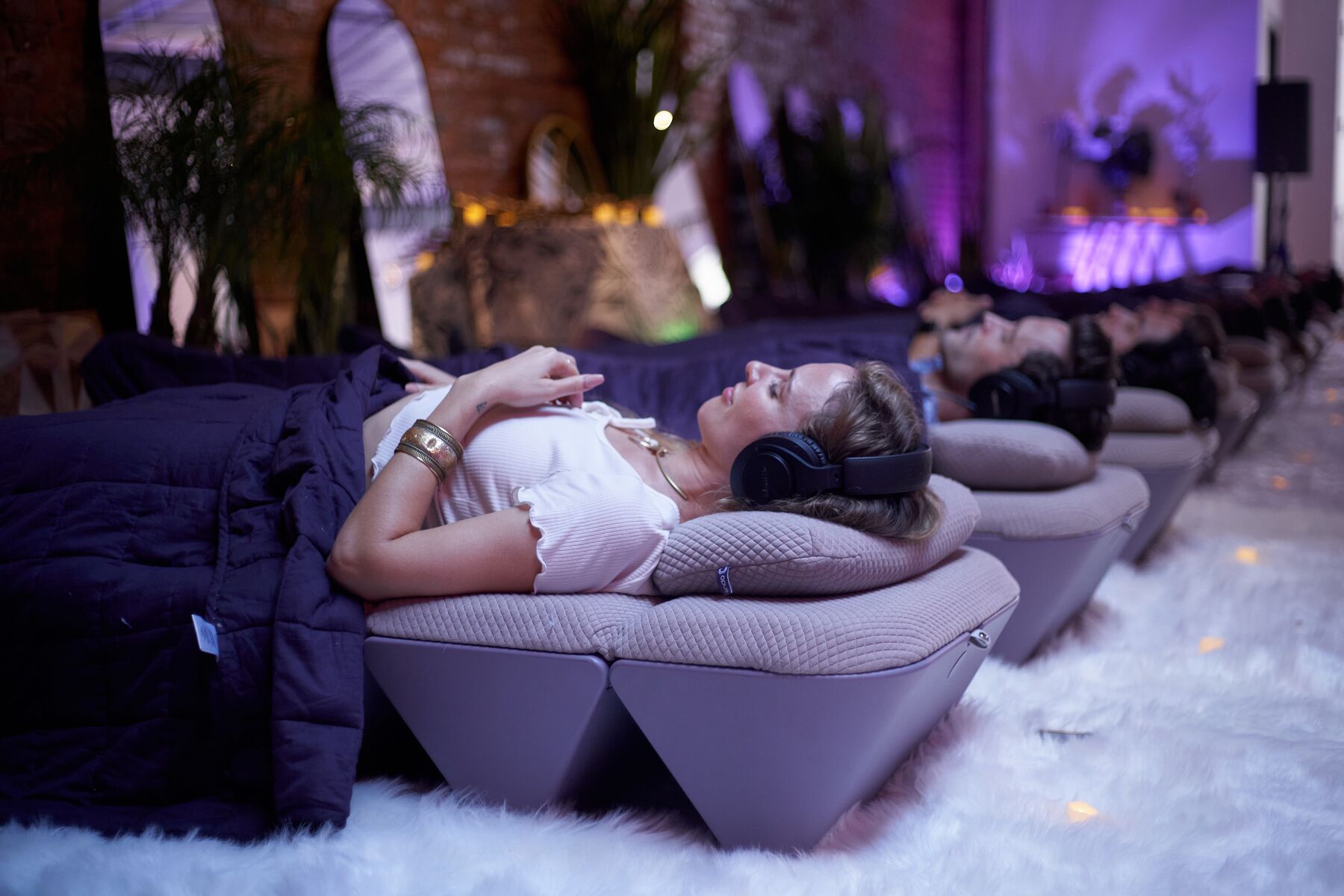 Guests reclined on AVA under headphones, blankets pulled up, the room lit violet.