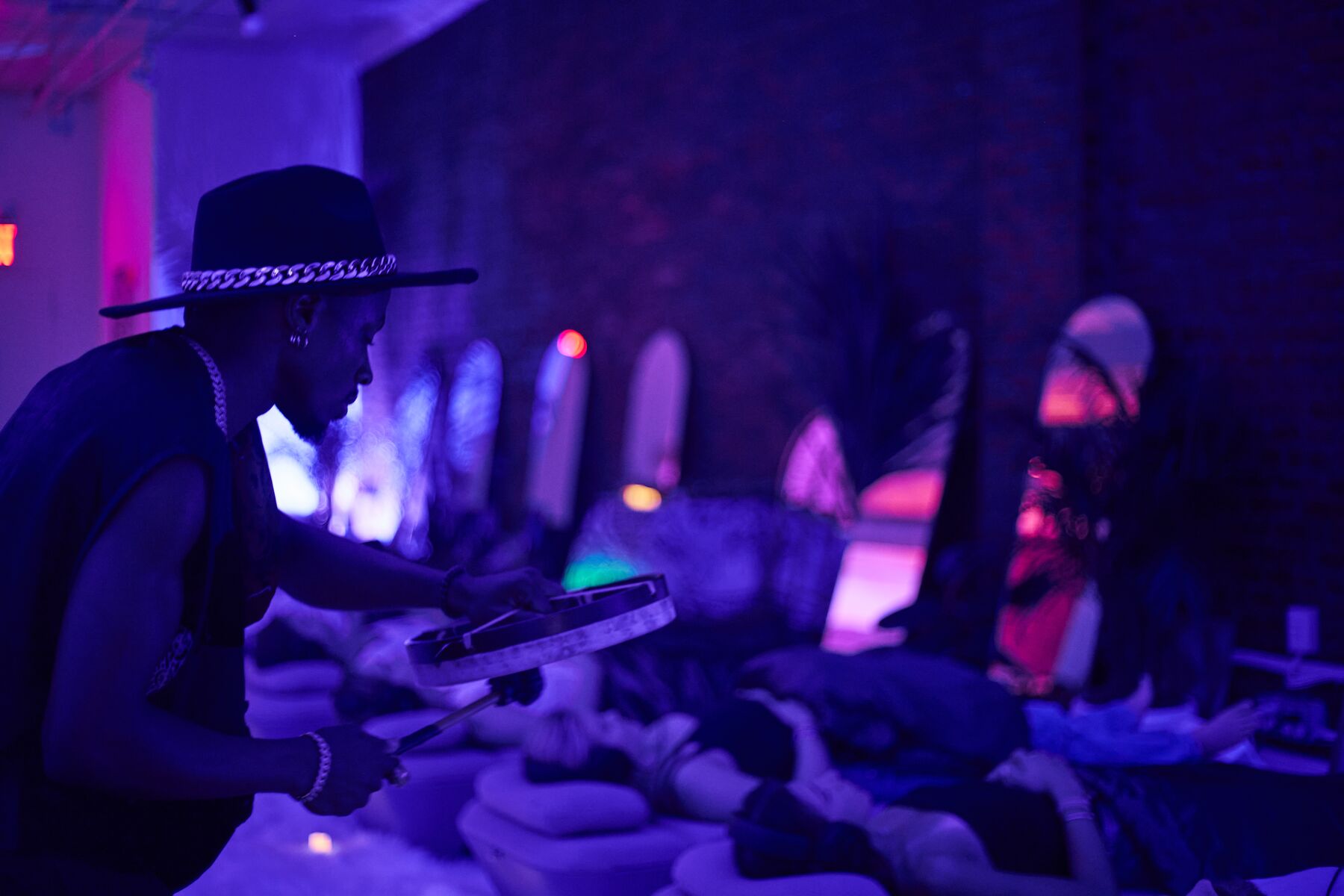 A drummer plays a frame drum over guests lying on AVA in deep blue light.
